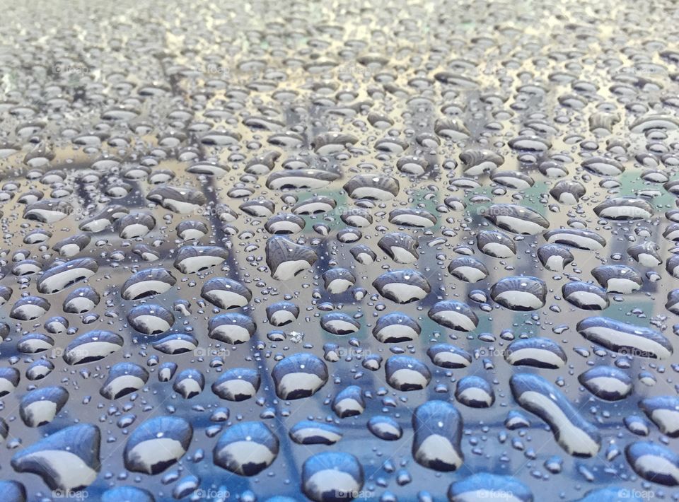 Water droplets on top of reflective blue surface showing outline of house and many windows. 