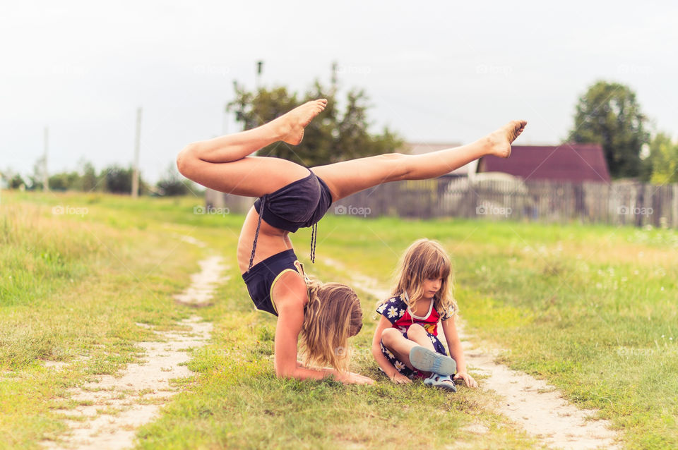 Girl doing yoga with her little sister on the countryside