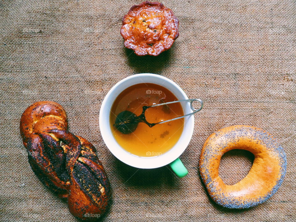 bagel with poppy seeds, basket with poppy seeds, vanilla cupcake and a cup of tea on the table