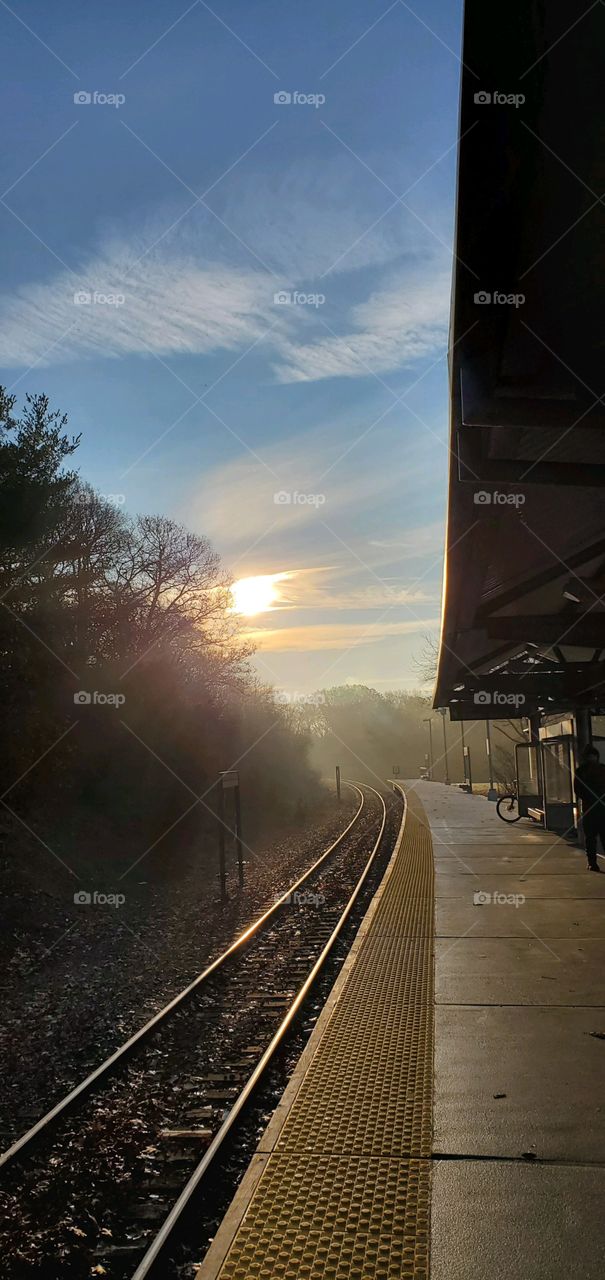 Sun rising over train tracks in early morning. Waiting platform empty after train just left picking up passengers for commute to City.