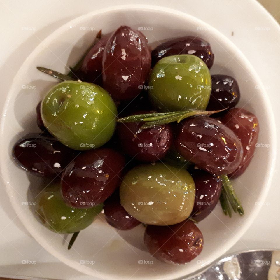 Delicious oiled green, black and brown olives served in a white dish.