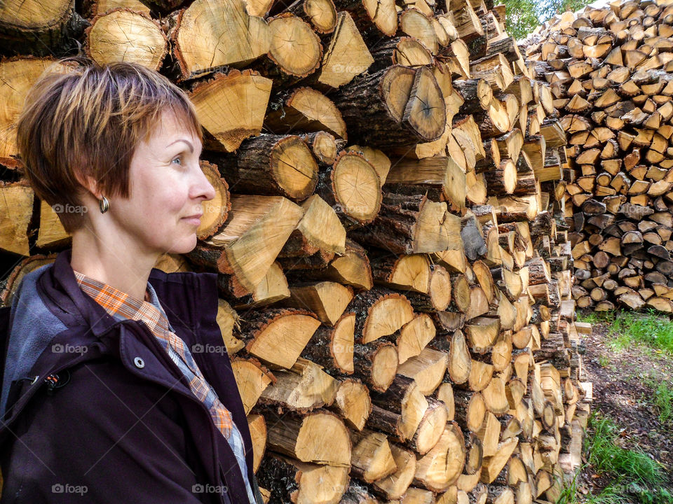 Portrait of woman standing near wooden stack