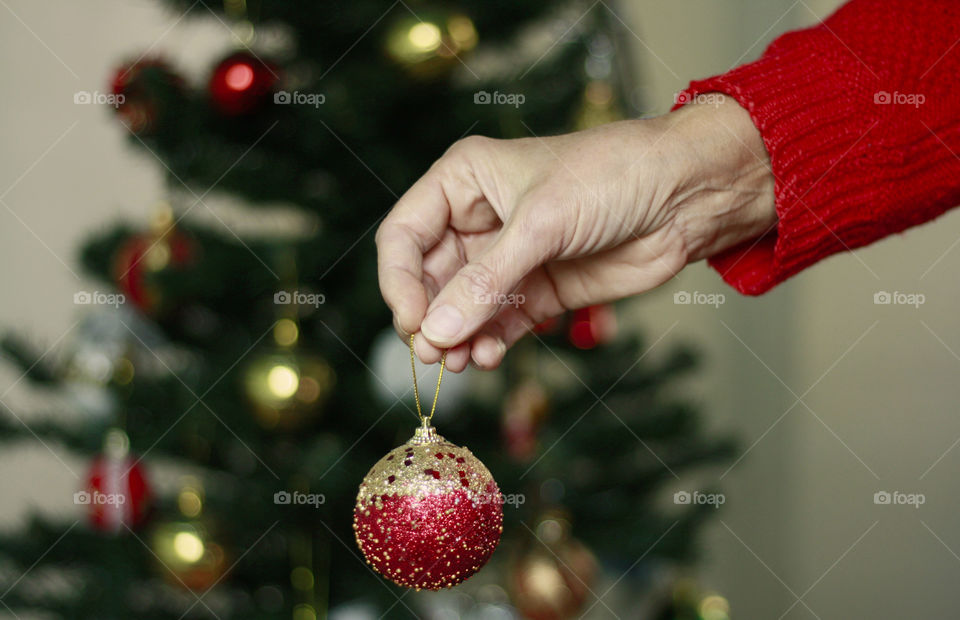 A hand holding Chrismas ball, decorating a Christmas tree