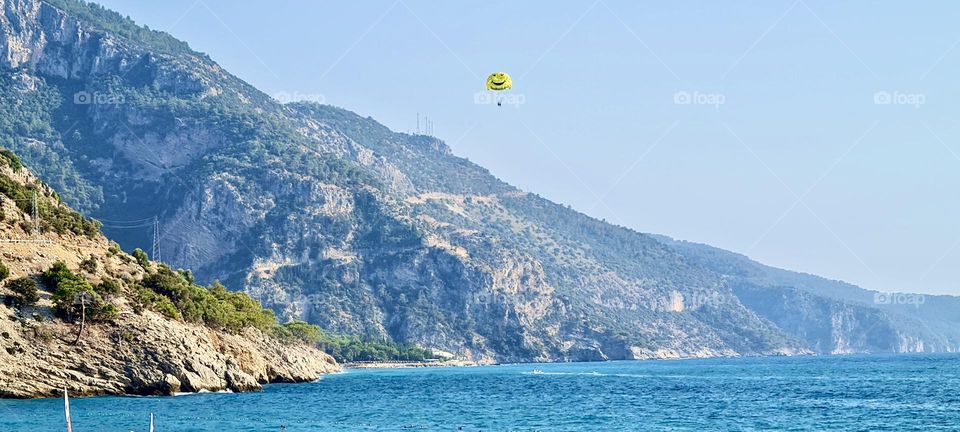 A parachute with a smiling face flies over the sea and mountains
