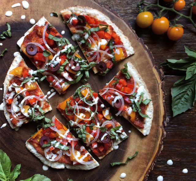 Pizza on flatbread with cherry tomatoes, onions, olives and fresh basil. 