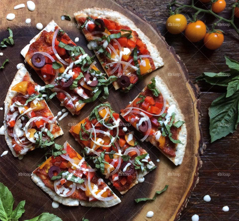 Pizza on flatbread with cherry tomatoes, onions, olives and fresh basil. 