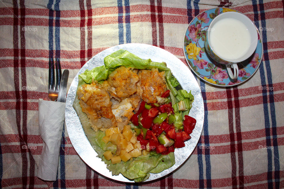 fish with vegetables and cheese on a tin plate with aizberg salad and a glass of yogurt on a colorful tablecloth