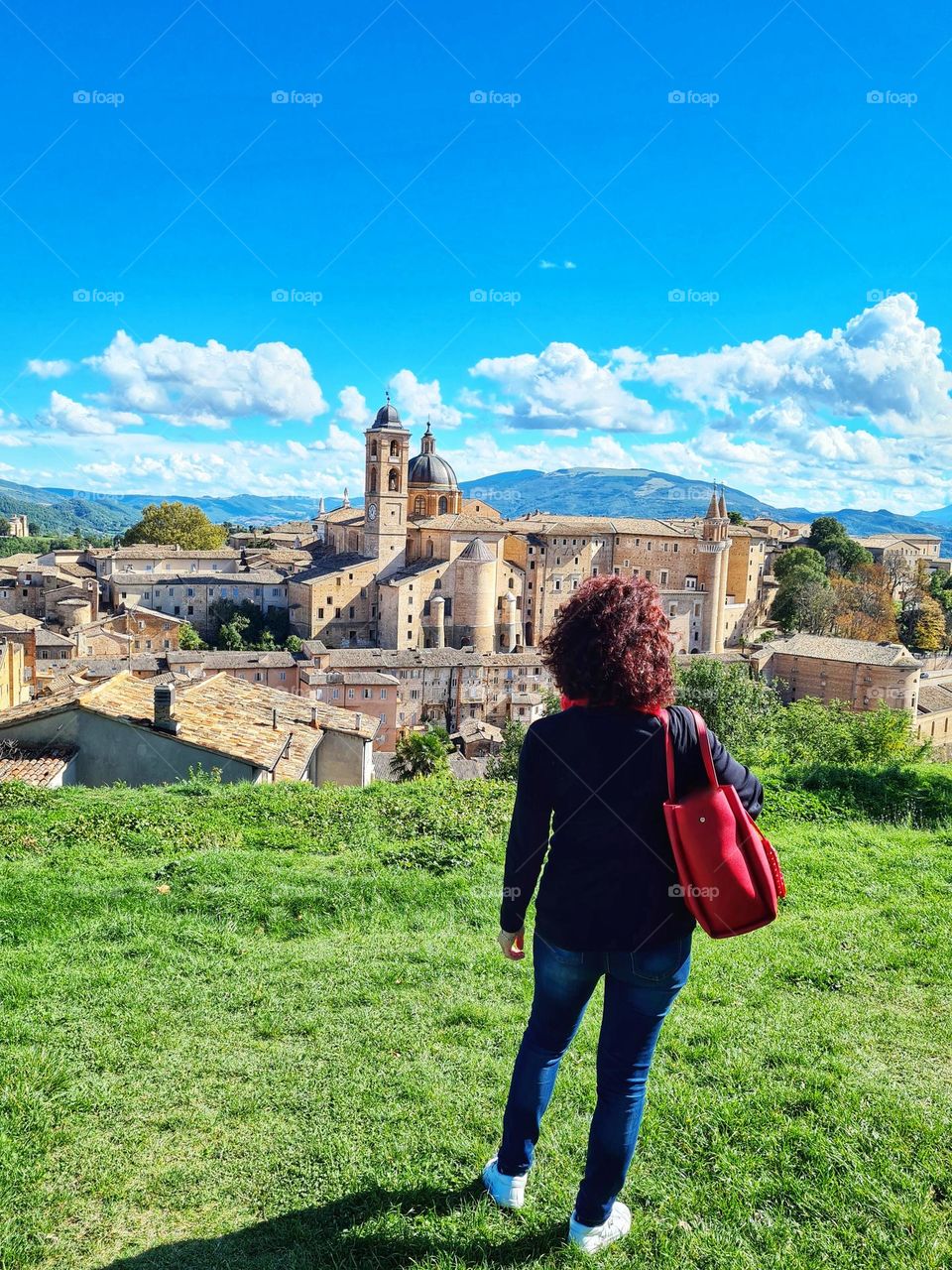 woman from behind observes the historic center and the cathedral of Urbino in Italy