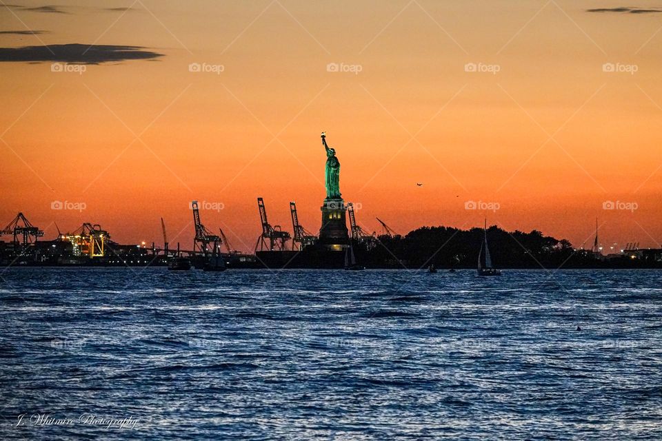A brilliant orange sunset is the backdrop for the Statue of Liberty in the New York harbor