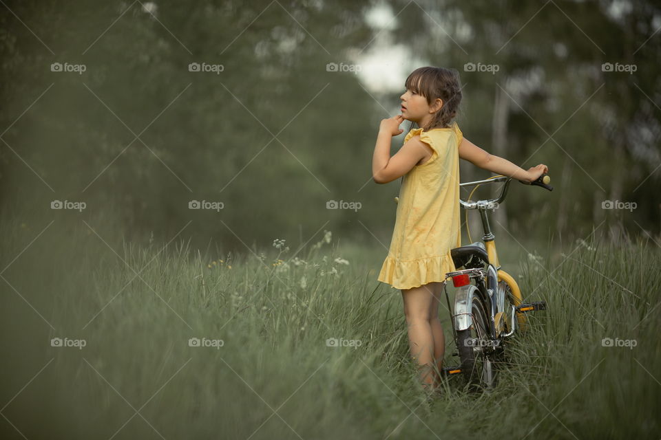 Little girl with bicycle in the summer field 