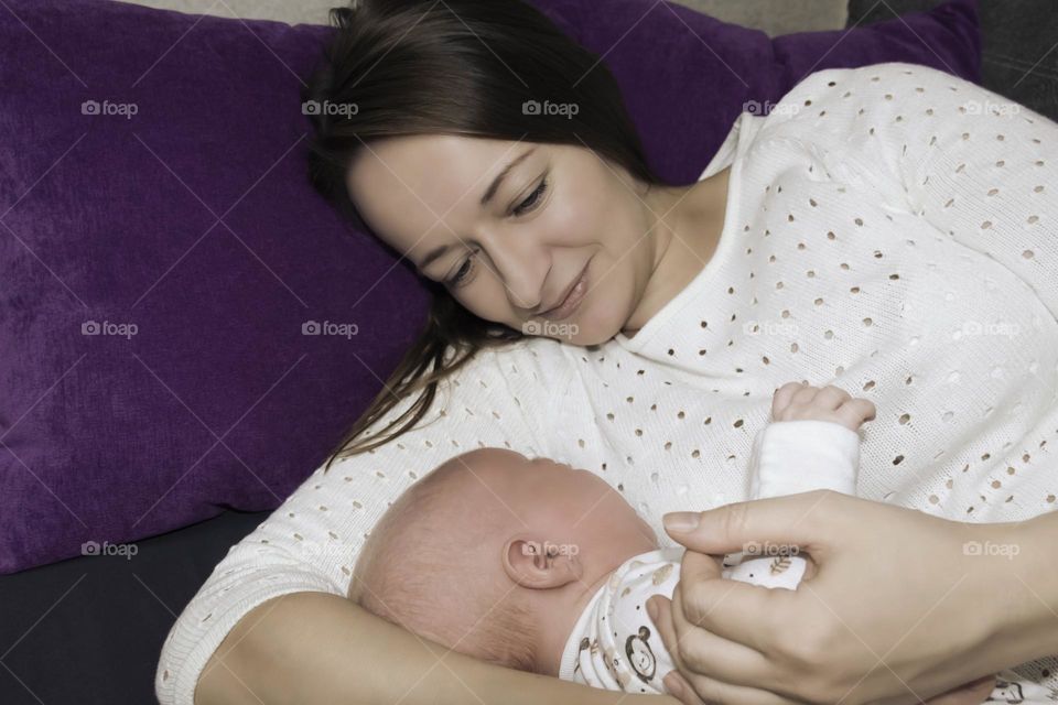 A young, happy mother lies in bed with a newborn baby.