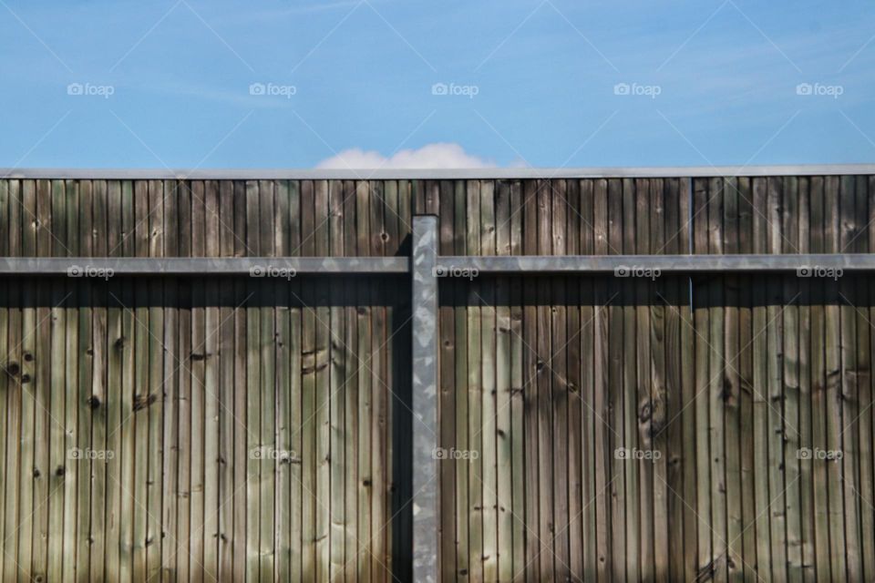 A small cloud standing behind a wooden fence in the blue sky