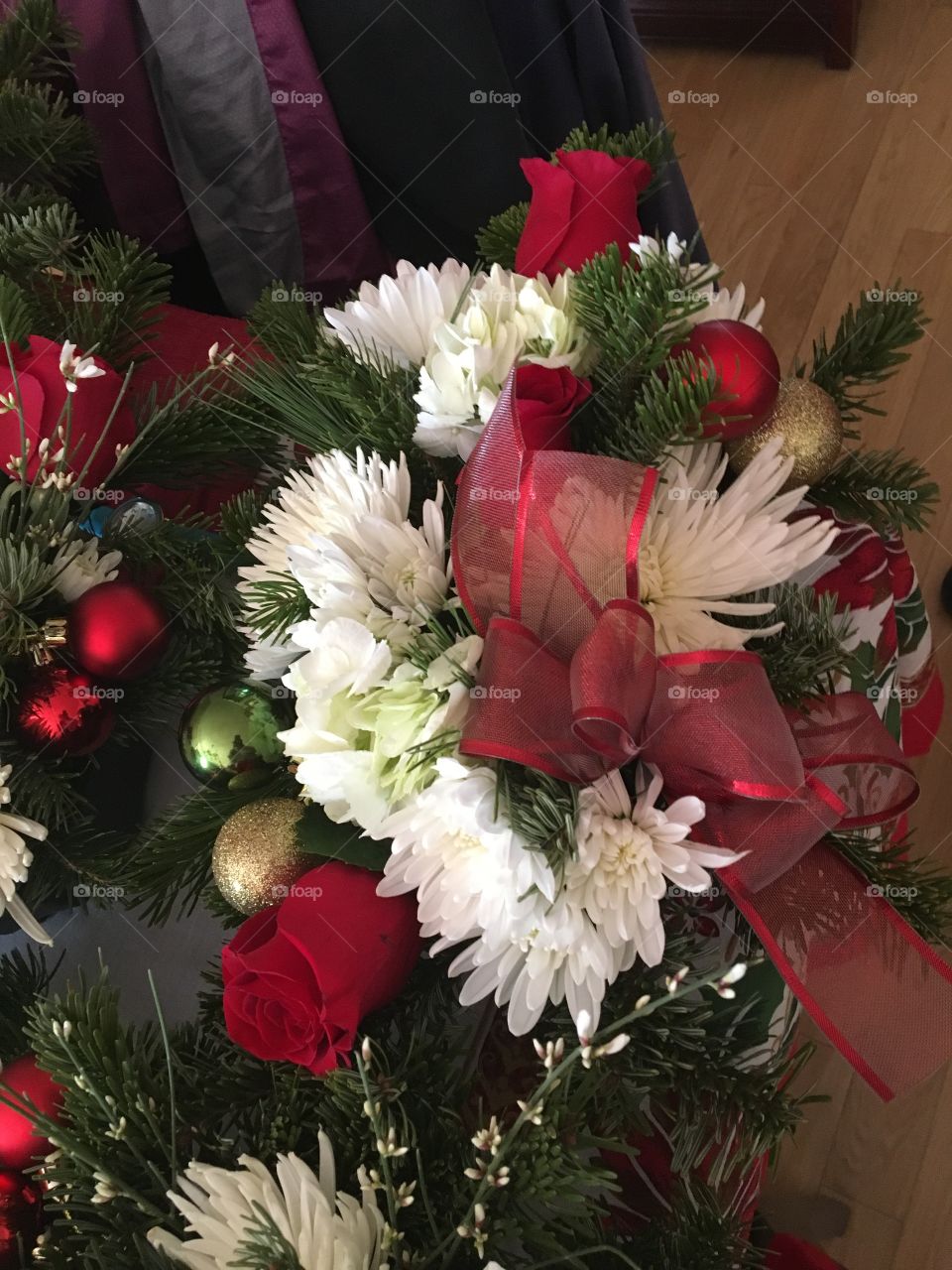 Red bow on Christmas centerpiece with green and gold Christmas bulbs. Red roses green pom-pom pine needles