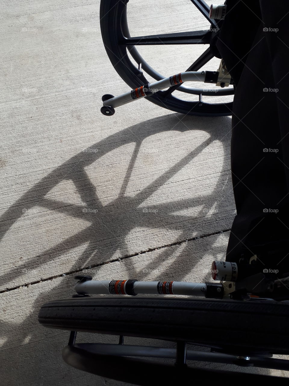 A wheelchair casting shadows of it's wheels along the street on the sidewalk in town.