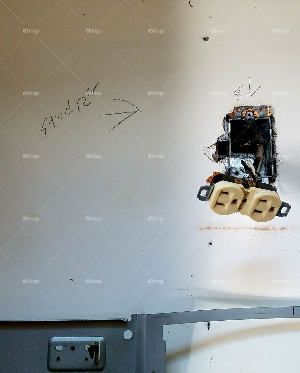 Electrical outlet hanging out from a hole in the wall, measurements are written by electrician on wall before installation is completed.