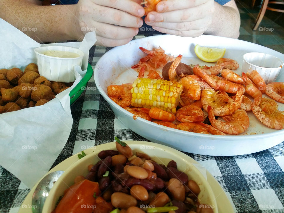 Cajun dinner of red beans and rice fried okra with ranch dressing corn and a man's hands peeling boiled shrimp in the Shell