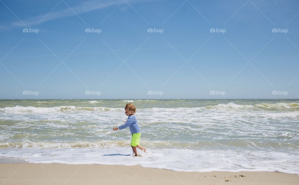 Little boy run at sea coast beach with waves and foam 