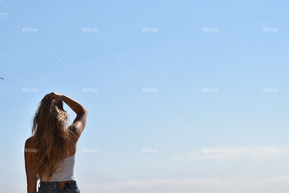 girl with hand in hair looking at blue sky wearing white top and jean shorts 