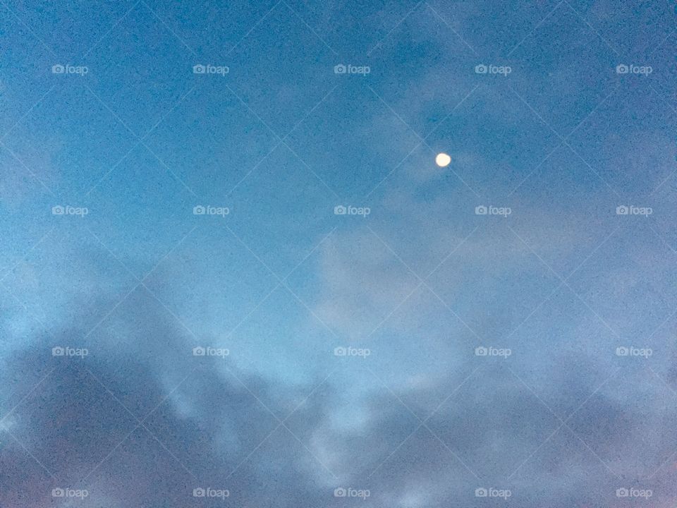 A gibbous moon in a clear blue sky above wispy clouds