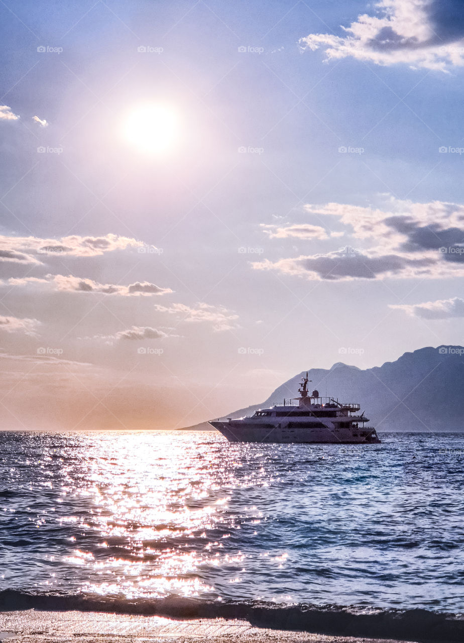 Sea summer landscape: a yacht in a calm sea on a background of sunset and mountains