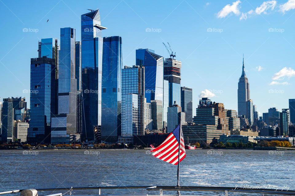 Taken from a ferry traversing the Hudson River in New York, the skyline of Midtown Manhattan along with the Empire State Building is visible along with a American flag