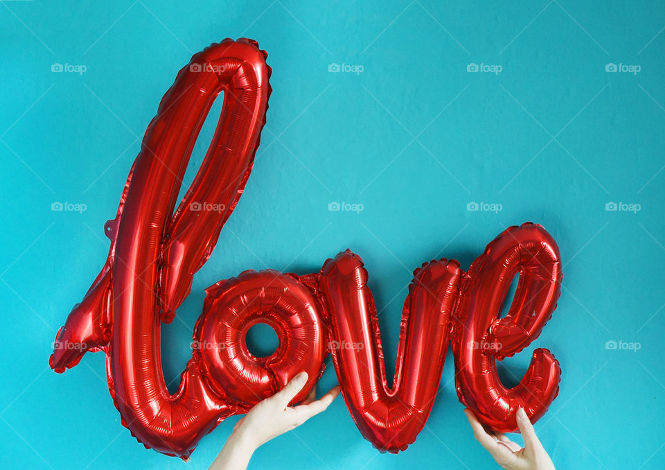 Red love word shaped baloon in girl's hands on blue background