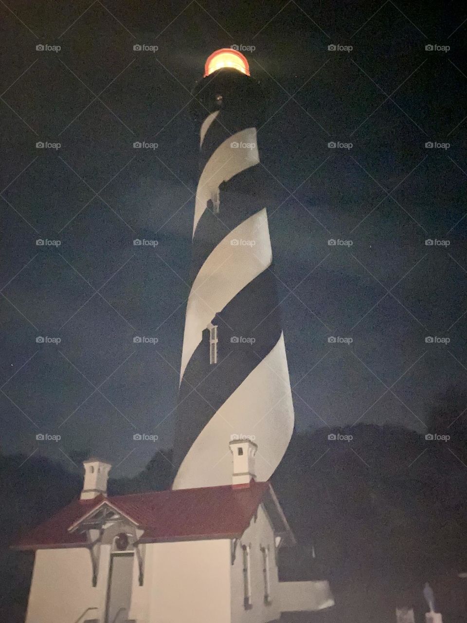 A black and white striped lighthouse against a misty night sky next to a small structure with a red roof