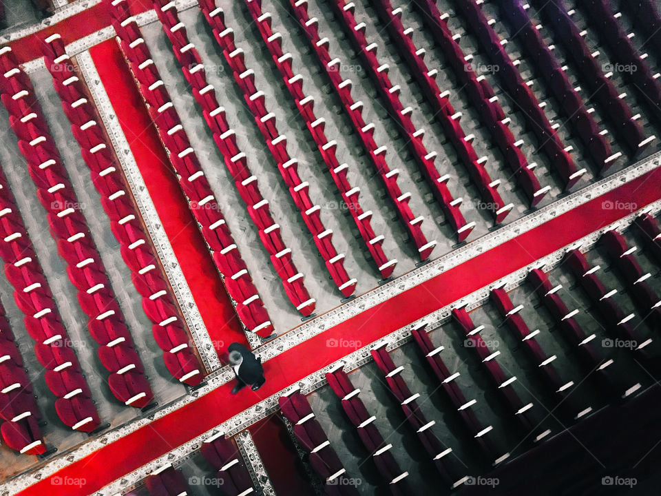 Overheard view of a Tiny human walking through the rows of red chairs in the theater 