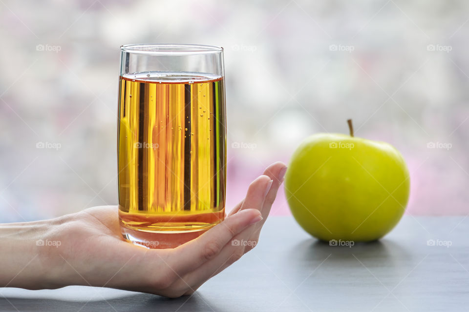 Human hand holding glass of juice near apple