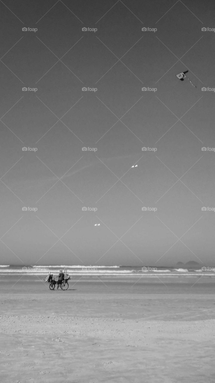 Beautiful Brazilian Beach, at Guarujá's EbsBeautiful Brazilian Beach, at Guarujá's Enseada Beach, sunny day . There's a Man with a cart, a bike, selling kieada Beach, sunny day . There's a Man with a cart, a bike, selling kites. Black and white shot.