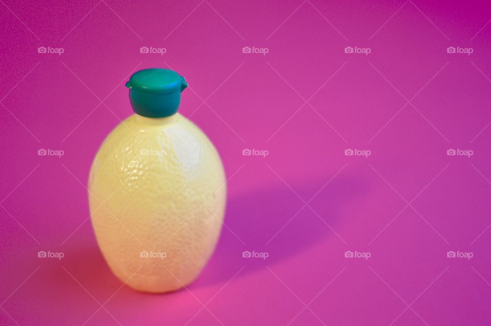Contrasting flatlay with a bright pink background and a yellow and green plastic lemon juice bottle 