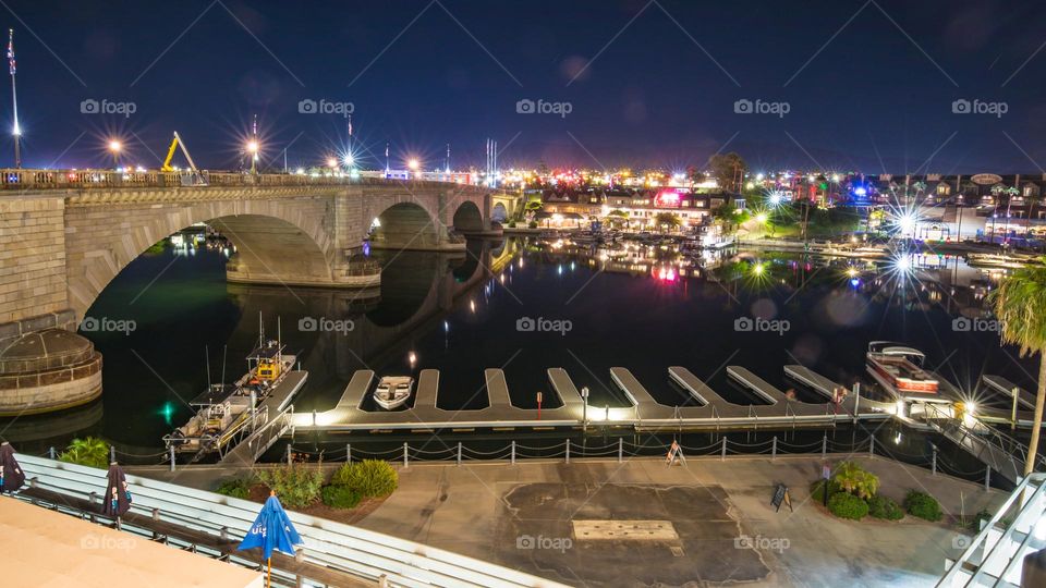 London Bridge in Lake Havasu City, Arizona, USA seen at night from a hotel balcony. Clear reflections on the water surface of Colorado River Canal. Boat docks to the front and downtown area on the other side of the bridge.
