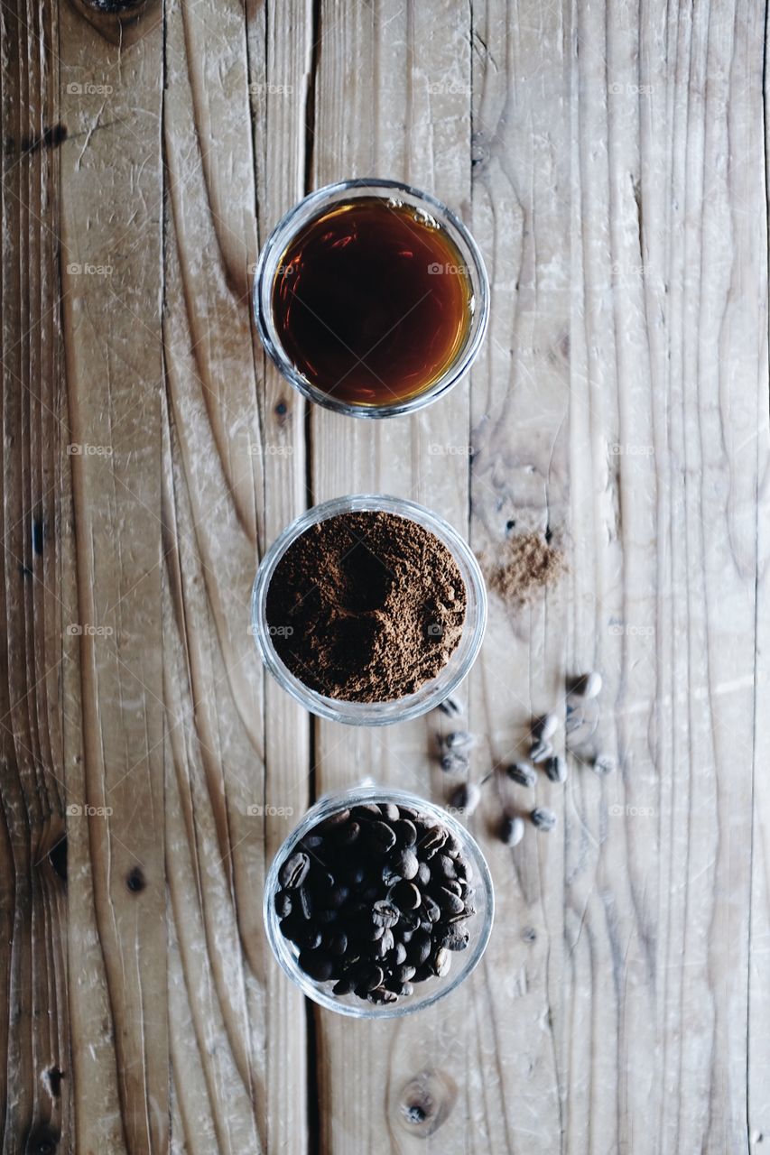 Three glasses on a table showing the progression and process of coffee making. Window light shining on the table. 