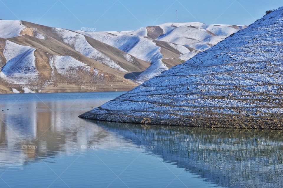 the foot of the mountain is reflected in the waters of the mountain lake dot in the background of the snow-capped peaks of the mountains. Pamir mountains in early spring.