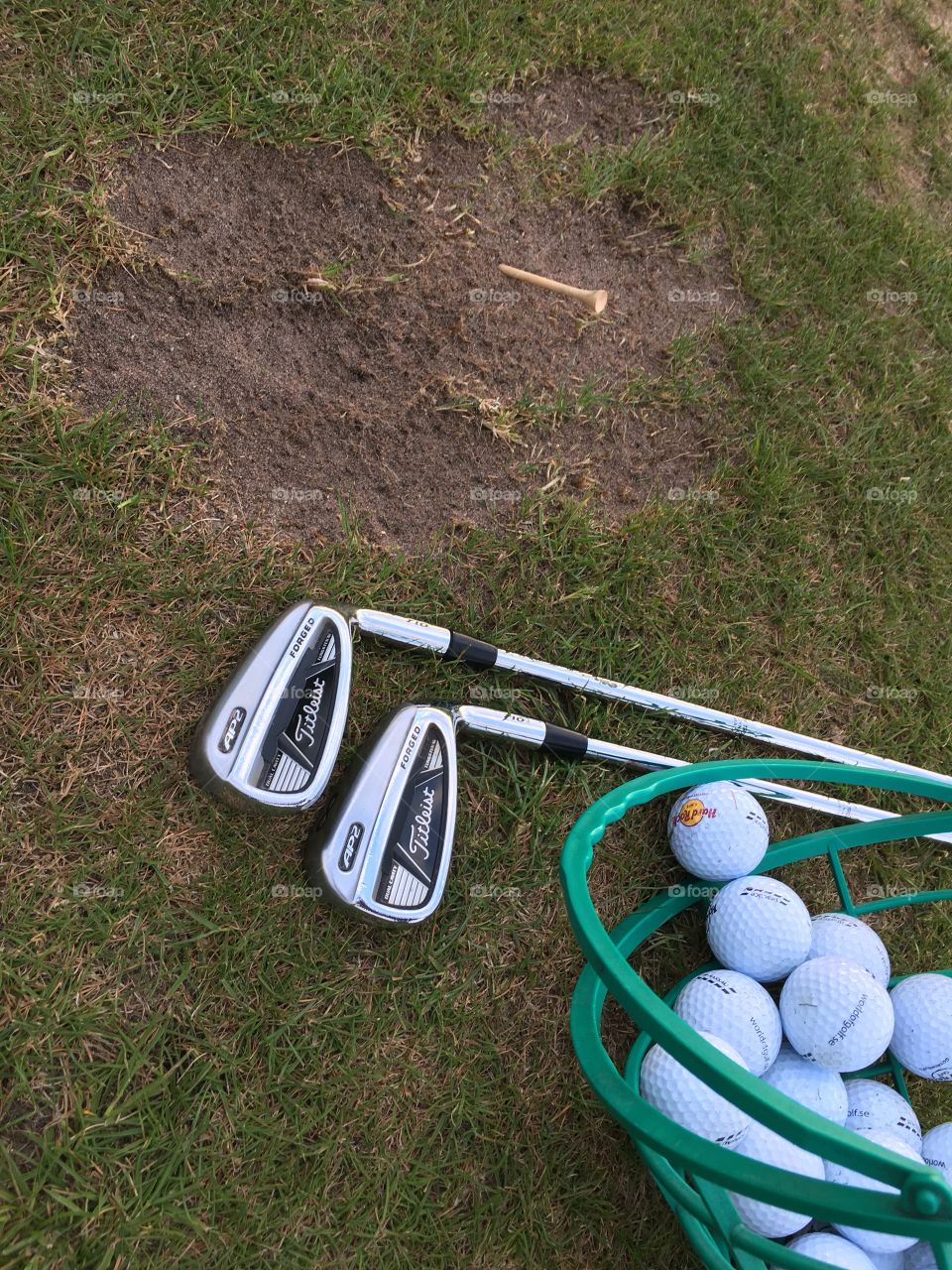 Titleist iron golf clubs and a bucket of driving range balls on the grass surface