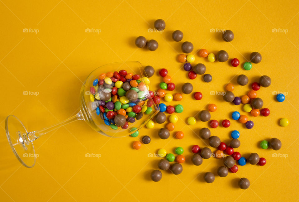 Sweet colorful candies in a glass on yellow background