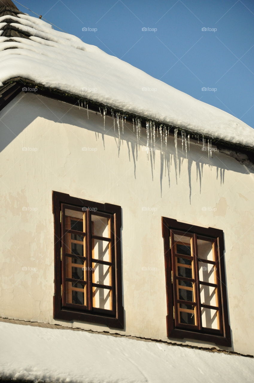 icicle hanging from roof of snow covered    building with two window in sunny winter day Wisla Poland