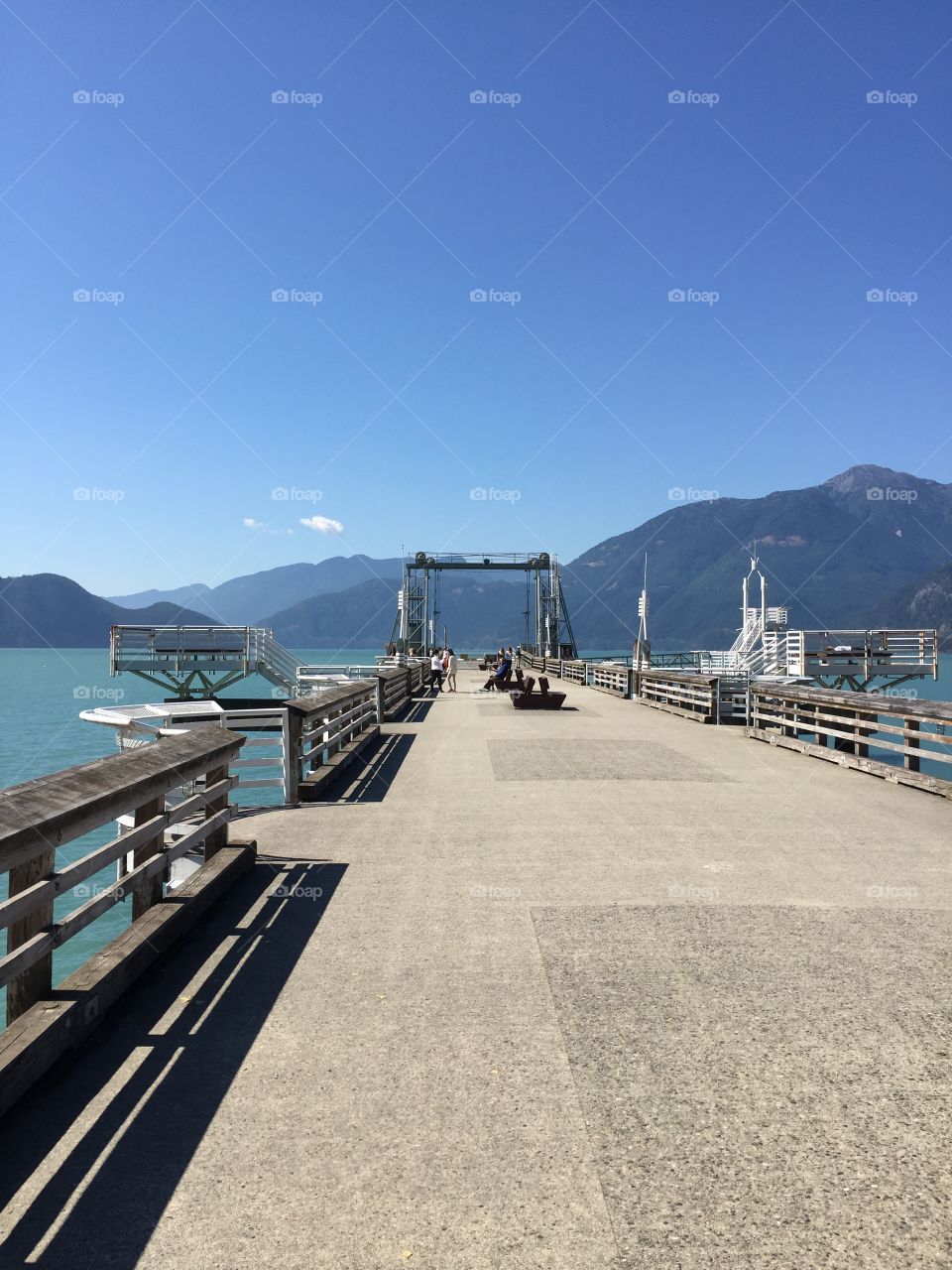 The pier at Porteau Cove with the Sunshine Coast in the background and little clouds in the sky.