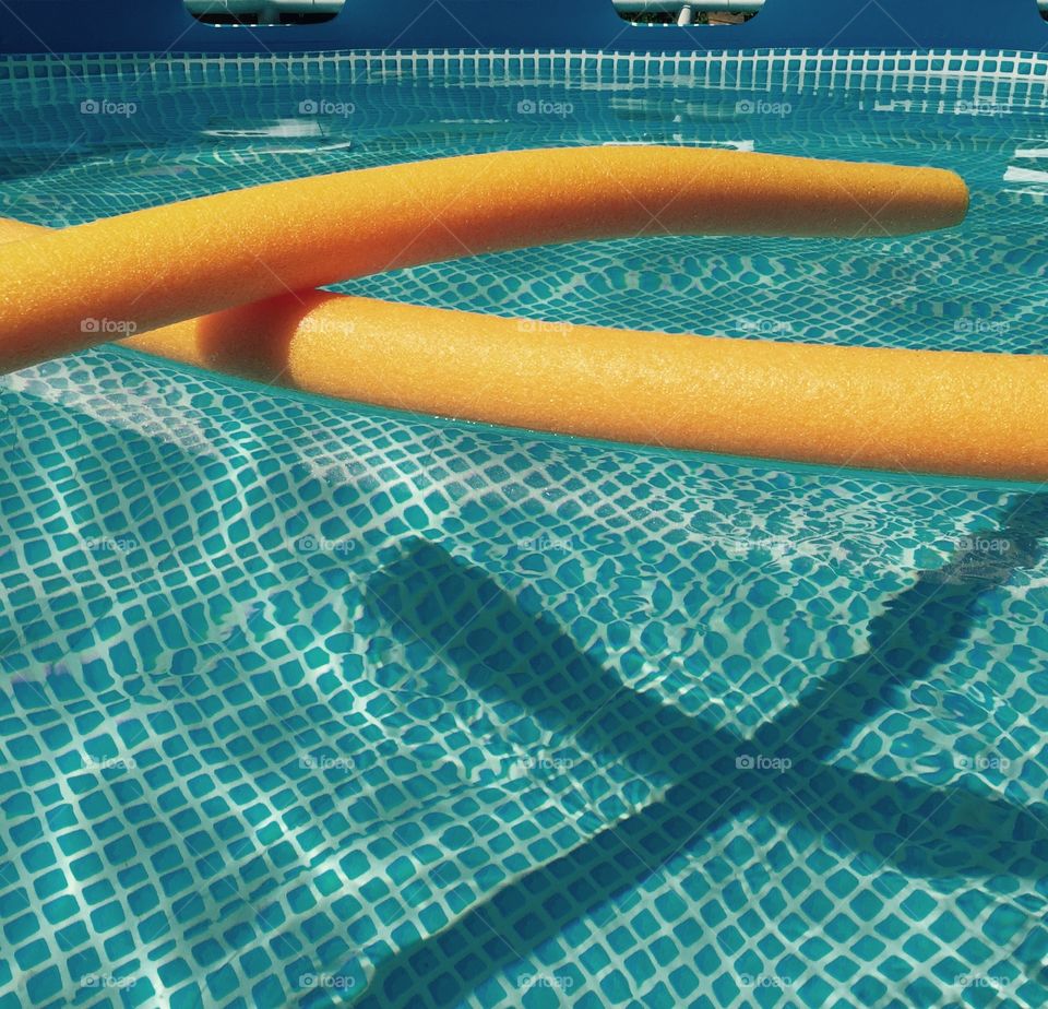 Two fat orange floating noodles that are for the pool floating in our pool waiting for us to jump on them!