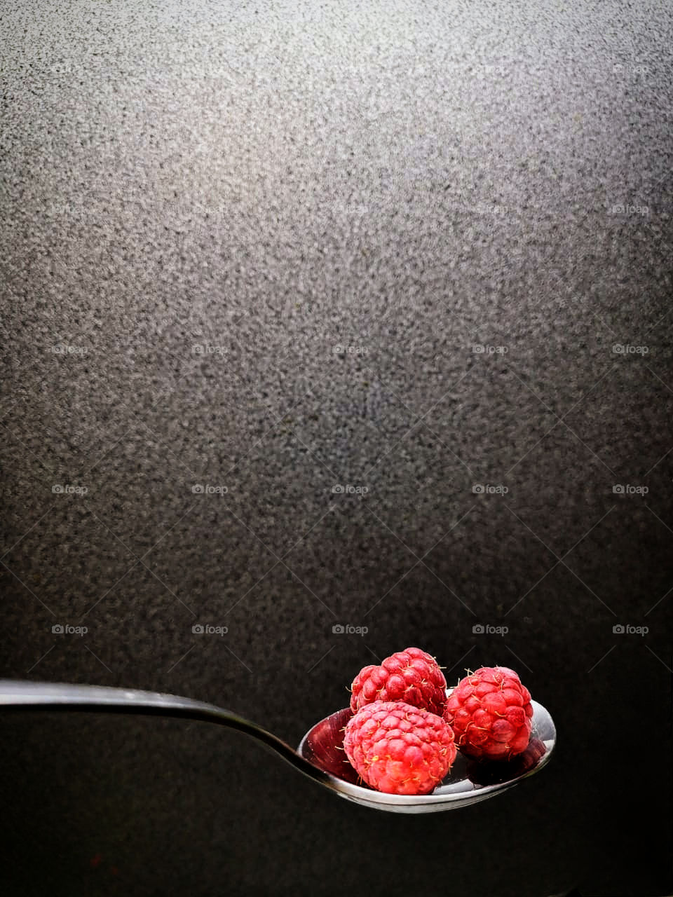 A metal spoon containing three raspberries