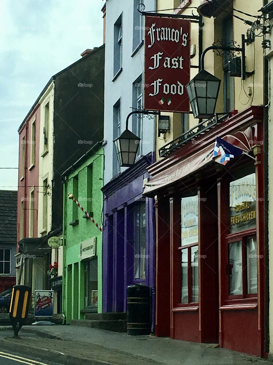 A lively scene on Main Street in Co. Clare, Ireland. The storefronts line the street in a vibrant display of color, each one unique and inviting. The entire street feels like a painter's palette, making the street feel welcoming and distinctly Irish.