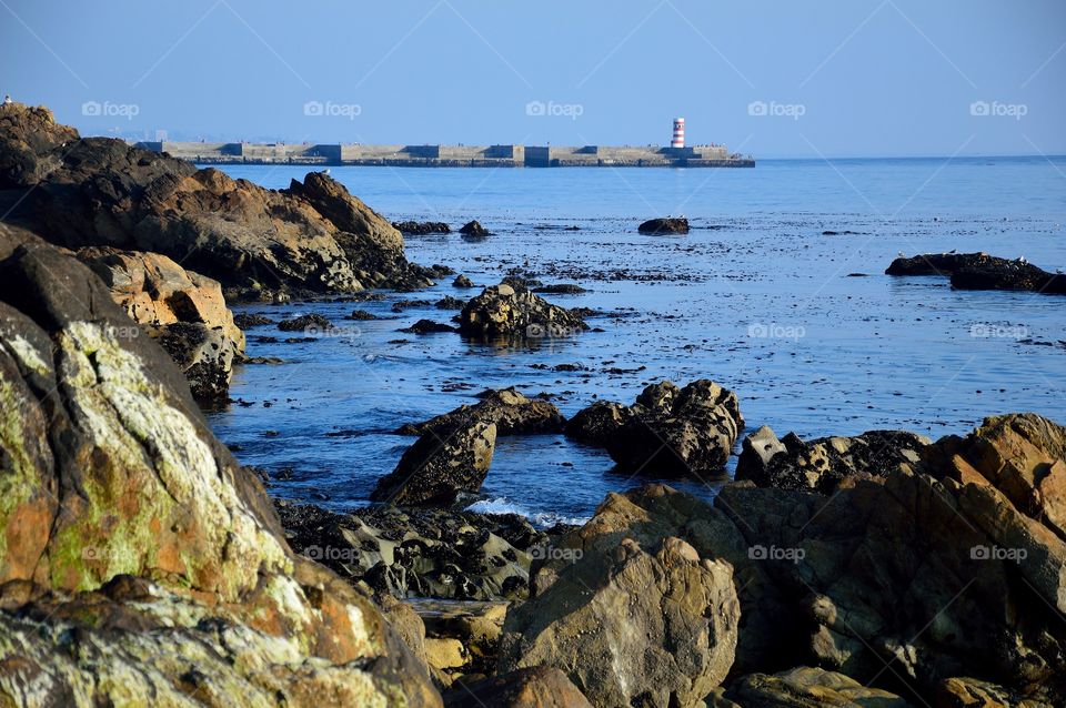 setting sun on the shore with lighthouse in the background