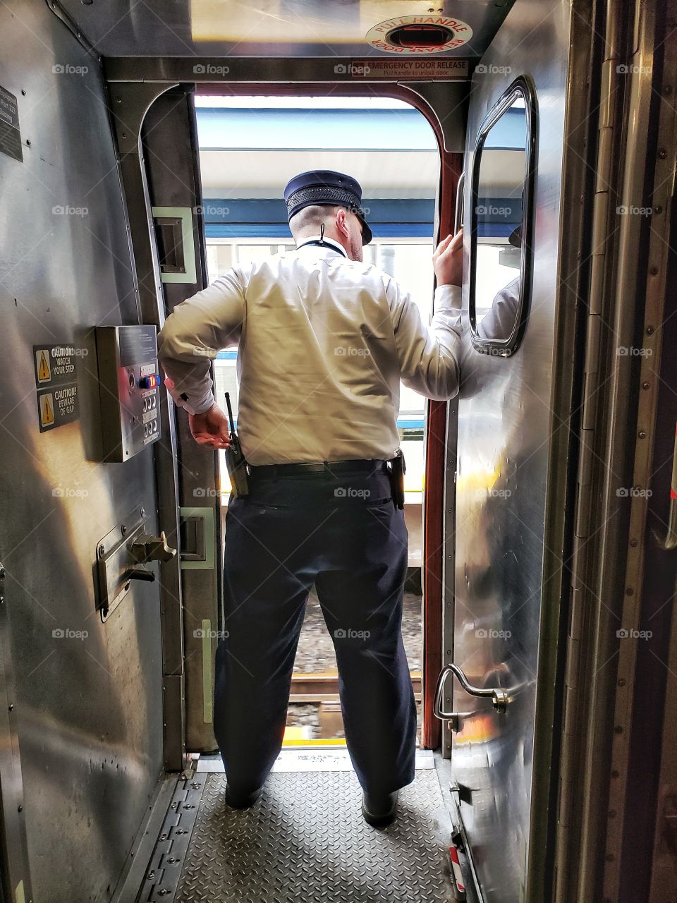 A male train conductor stands in an open doorway.