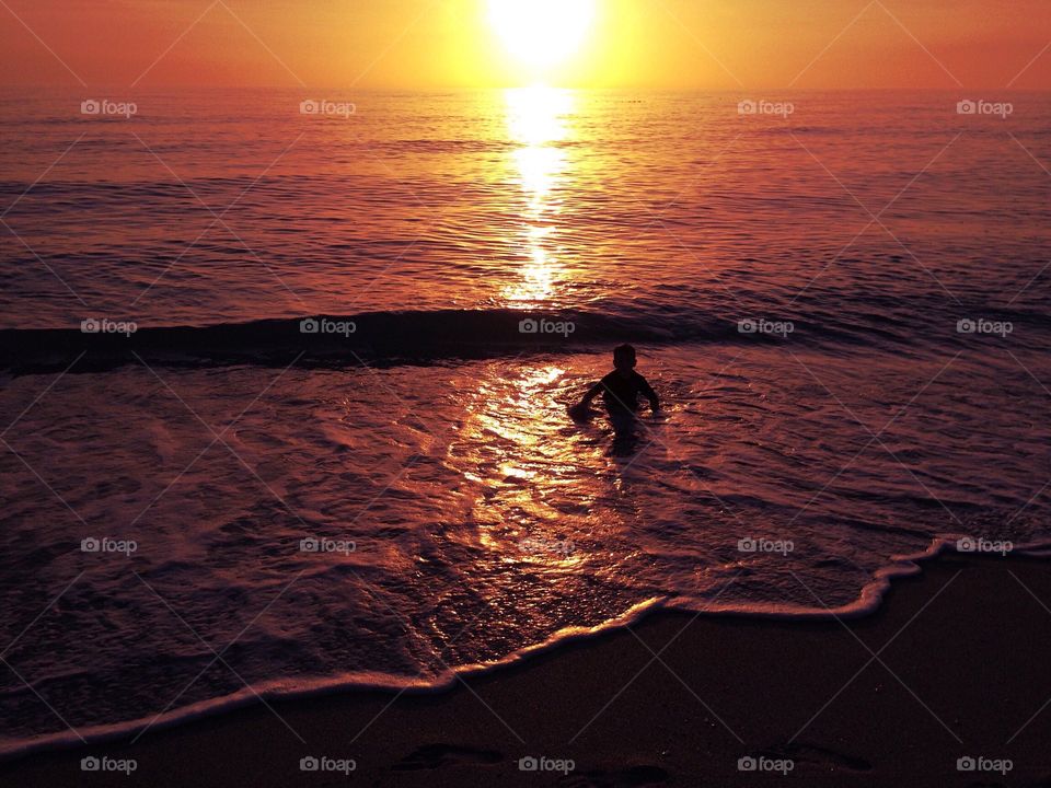 Small boy in the ocean surrounded by a golden sunset.