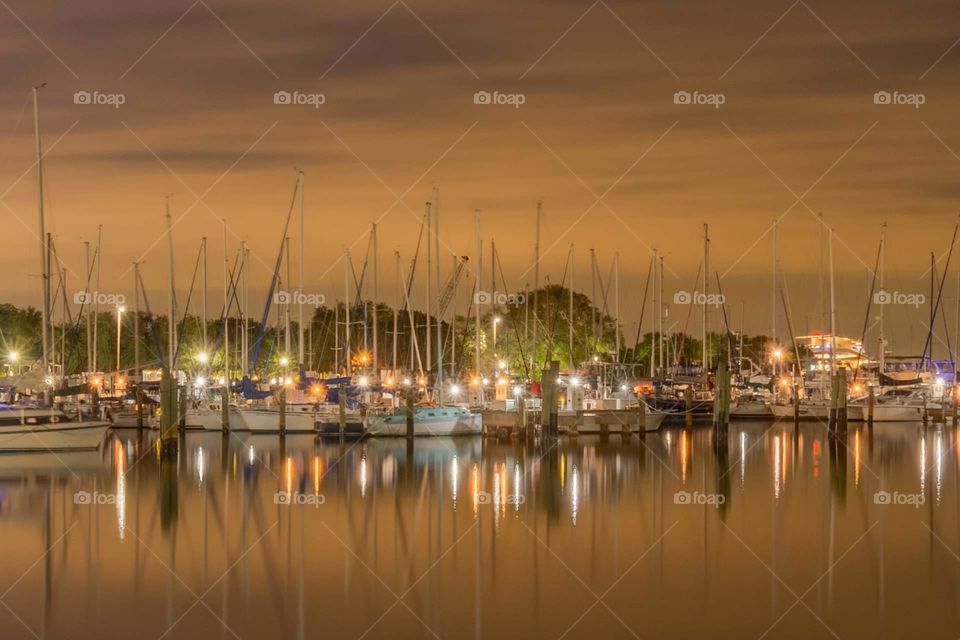 warm night image of small boats all docked together in a marina at sunset against an dark orange sky and reflected in the smooth water