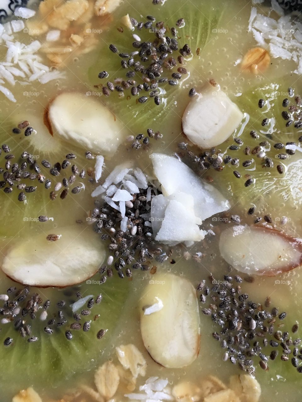 Full frame closeup healthy eating background photography of green fruit smoothie bowl ingredients with kiwi, coconut, chia seed, almond, and oatmeal 