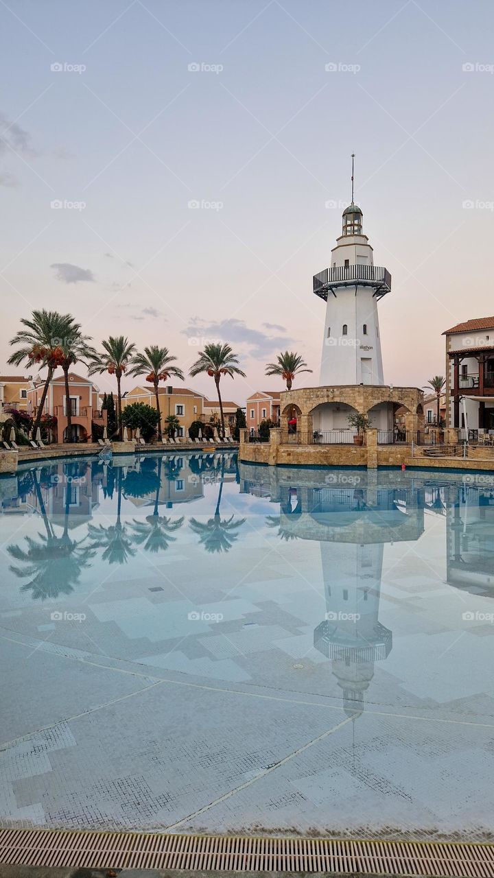 A lighthouse near a swimming pool. Pharoah reflection in water. Beautiful sunset sky