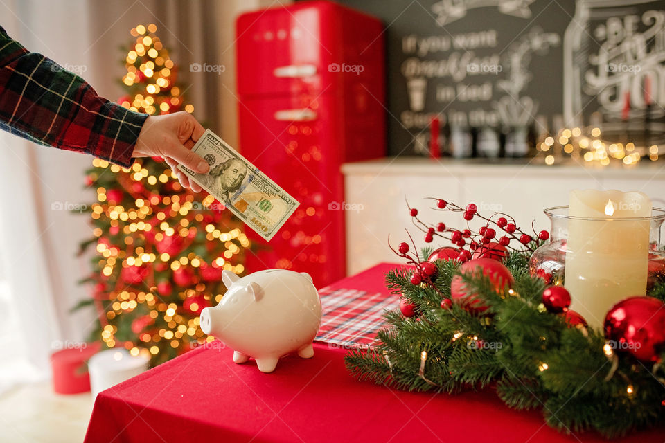 piggy bank with 100 dollars banknote in festive New Year atmosphere of scenery.  Magical bokeh with Christmas tree and bright lights.