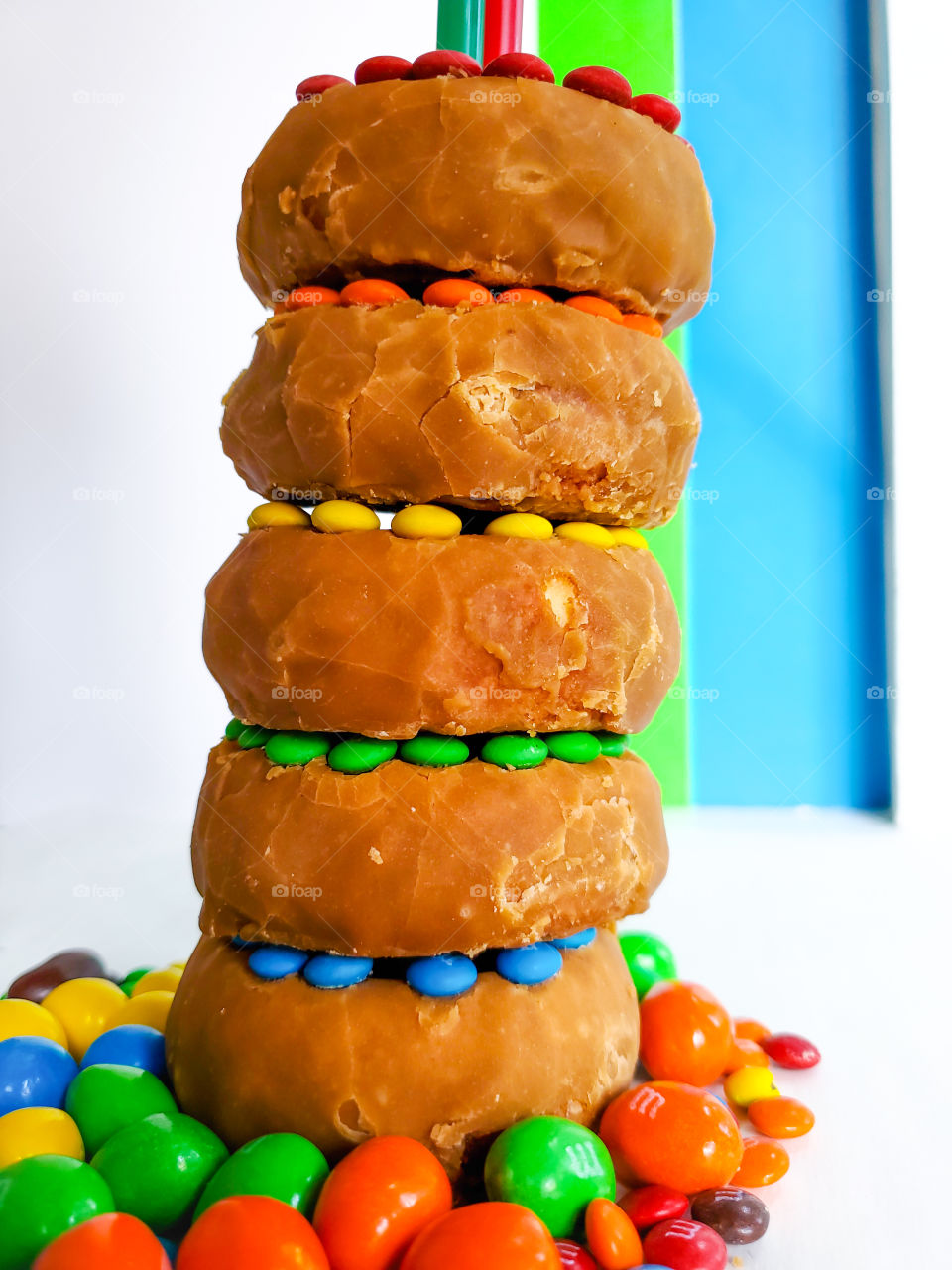 Stacked donuts decorated with M&M minis and surrounded by peanut M&Ms on a white surface with a blue, green and white solid background.  Reminiscent of the classic Fisher Price rock-a- stack infant toy.