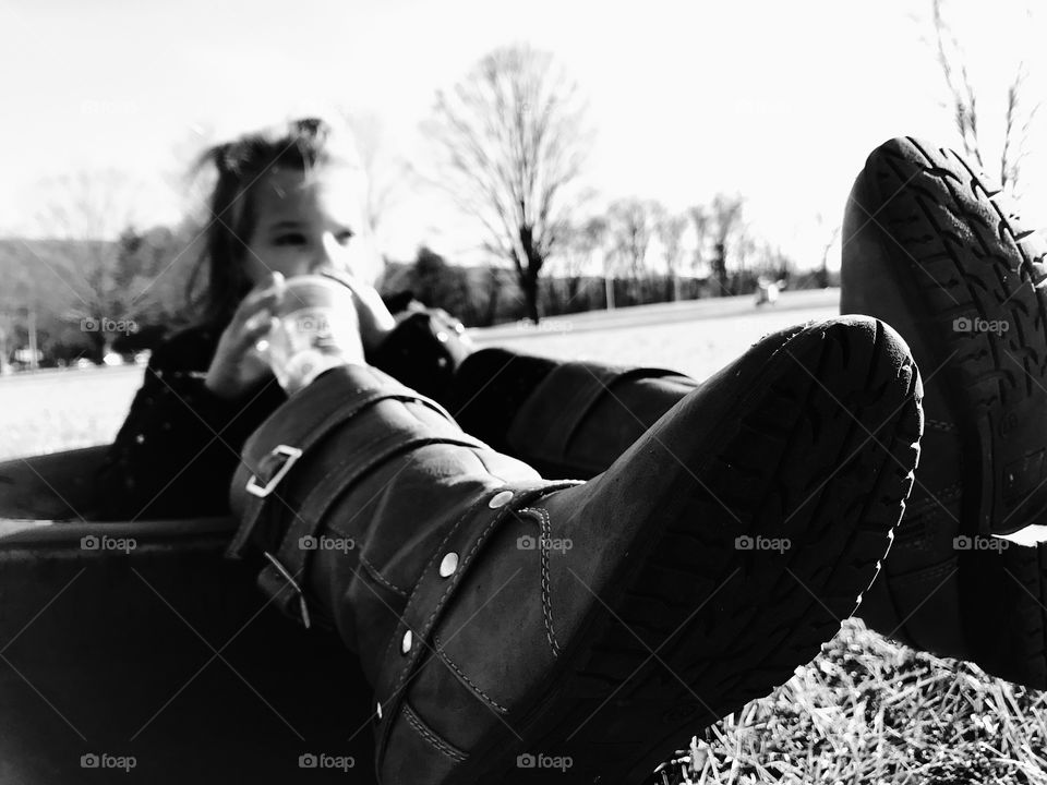 Black and white photo from an abstract perspective of a little girl with boots on sitting on the grass in the park. 